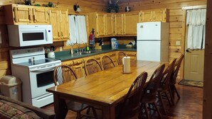 Uma cozinha no estilo de cabana de madeira, com mesa e cadeiras de madeira, micro-ondas, fogão e geladeira.