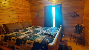 A wooden cabin room with a bed, a chair, a window with curtains, and a framed quote on the wall. - Bass - sleeps up to four (Moravia)