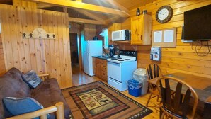 A cozy cabin interior with a sofa, a dining table, a kitchen area with a stove and microwave, and a television mounted on the wall. - Bass - sleeps up to four (Moravia)