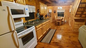 Interior de una cabaña de madera con cocina, comedor y sofá.