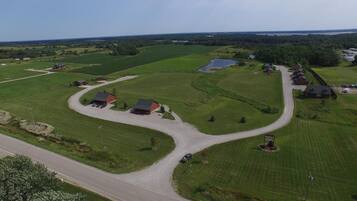 Ländliche Landschaft mit einer kurvenreichen Straße, grünen Feldern und mehreren Gebäuden mit roten Dächern.