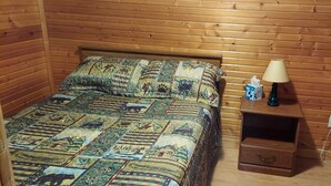 A wooden-paneled room with a bed, a nightstand with a lamp, a tissue box, and a dresser.