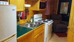 A compact kitchen with a refrigerator, stove, sink, and wooden cabinets.