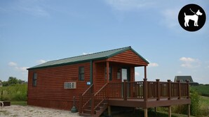 A wooden cabin with a porch and a deck, surrounded by greenery.