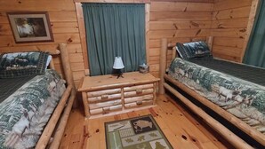 A cabin-style room with two wooden beds, a small table with drawers, a lamp, and a framed picture on the wall. - Elk - Sleeps up to 6 (Moravia)