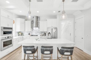A modern kitchen with white cabinetry, stainless steel appliances, a central island with bar stools, and pendant lighting. - ☀️Golf Cart-4 Bikes-2 Porches-30A-Time Out (Santa Rosa Beach)