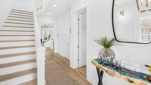 Un couloir avec un escalier en bois, des murs blancs et une console en marbre agrémentée d’objets décoratifs.