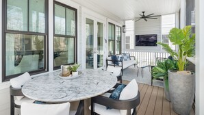 Une terrasse couverte avec une table ronde en marbre, des chaises blanches et un ventilateur de plafond.
