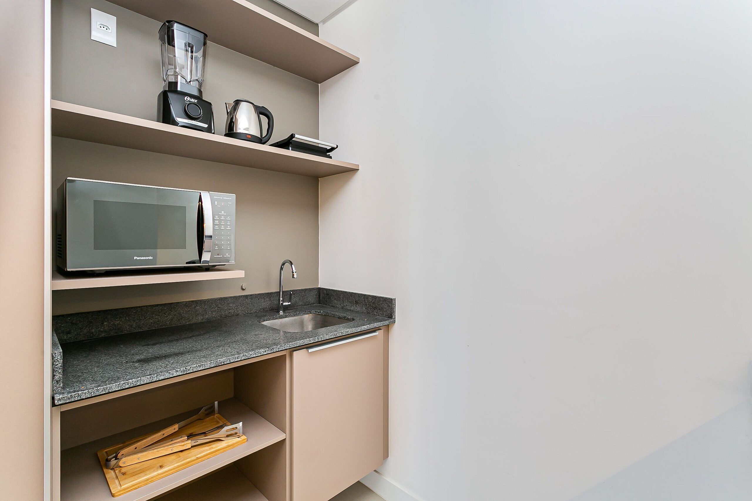 A compact kitchen with a microwave, coffee maker, and toaster on the countertop, and a sink with a faucet.