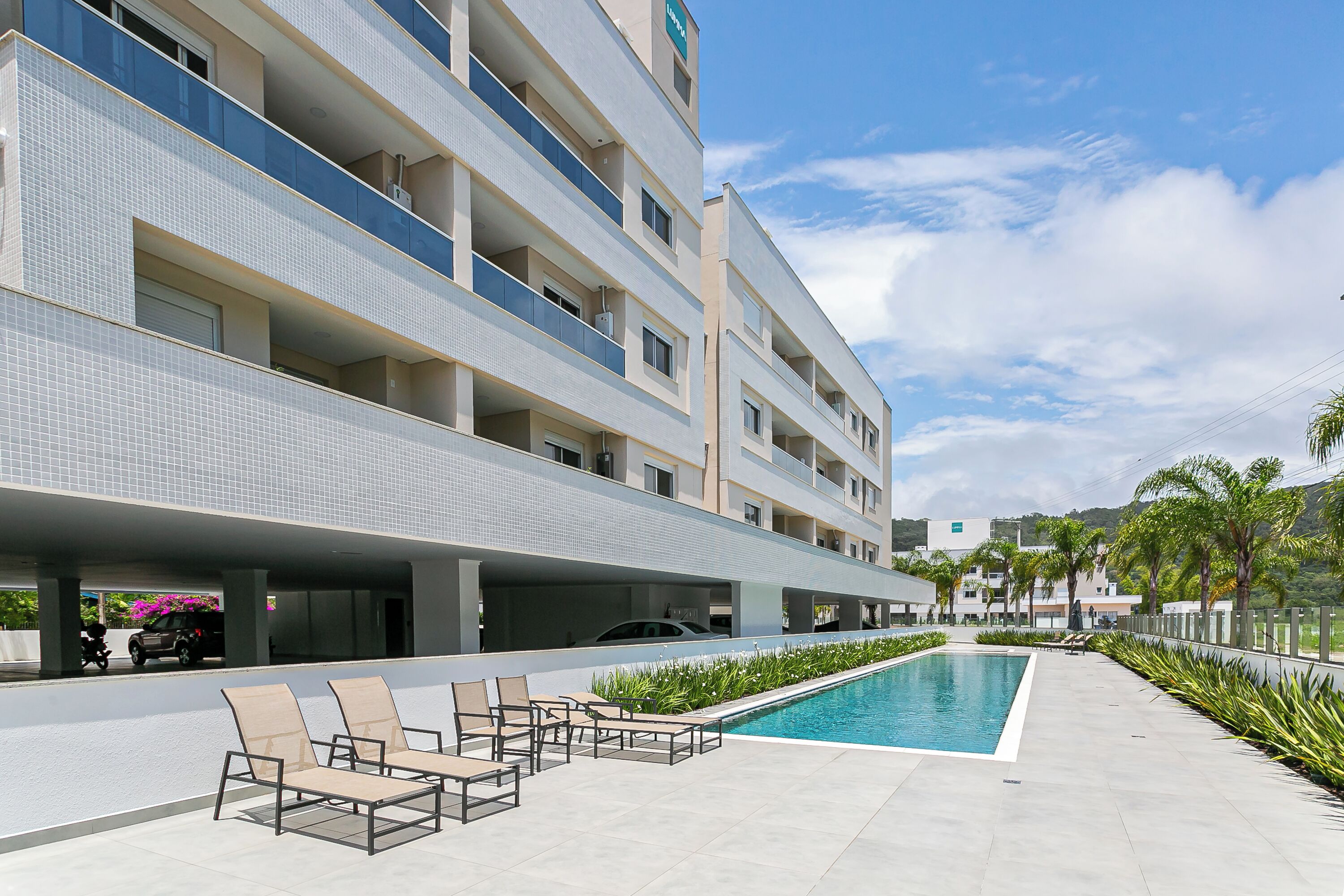 A modern hotel with a swimming pool, outdoor seating, and a covered parking area.