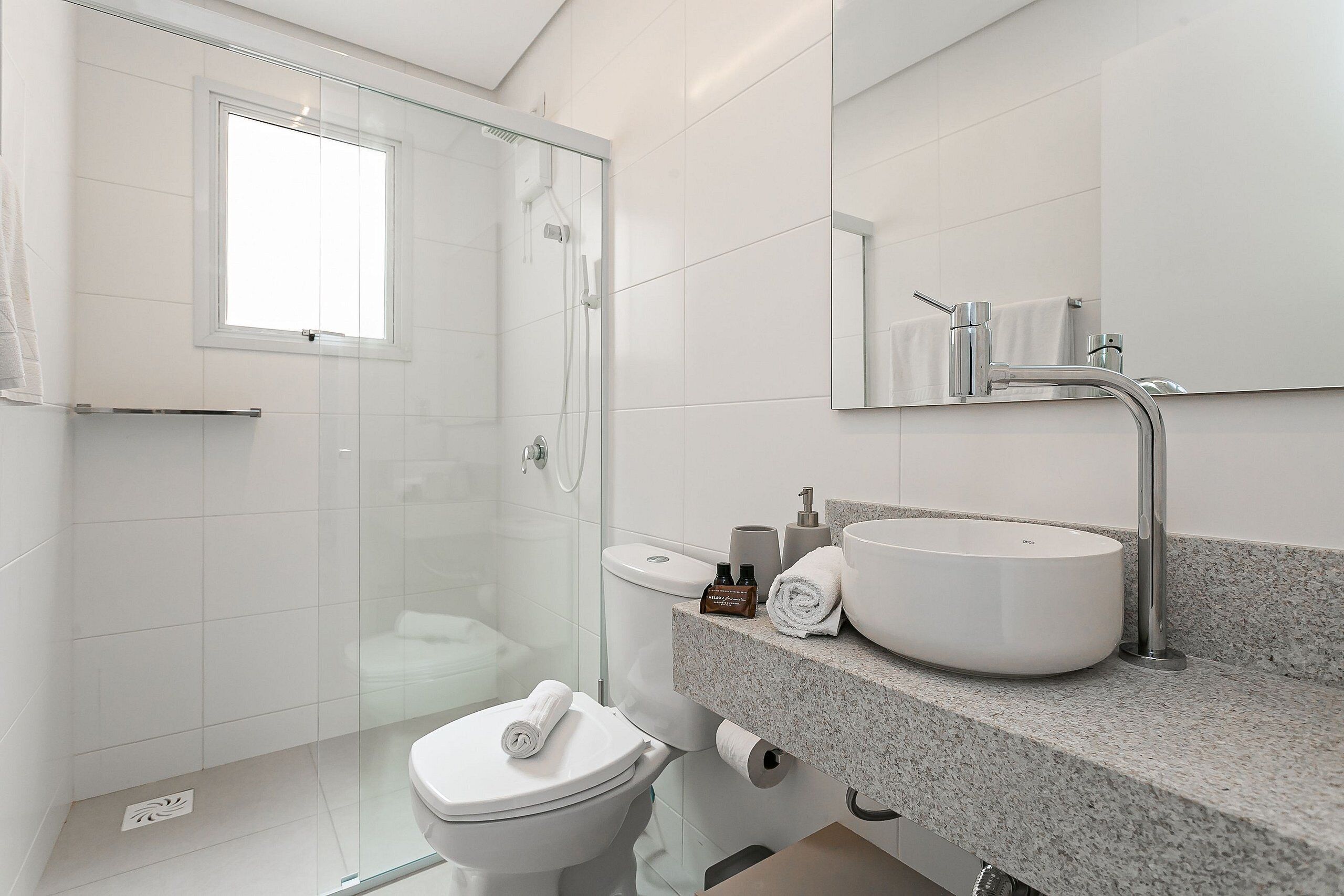 Une salle de bain moderne avec une douche à l’italienne en verre, des toilettes, un lavabo doté d’un grand bac et un miroir au-dessus du lavabo.