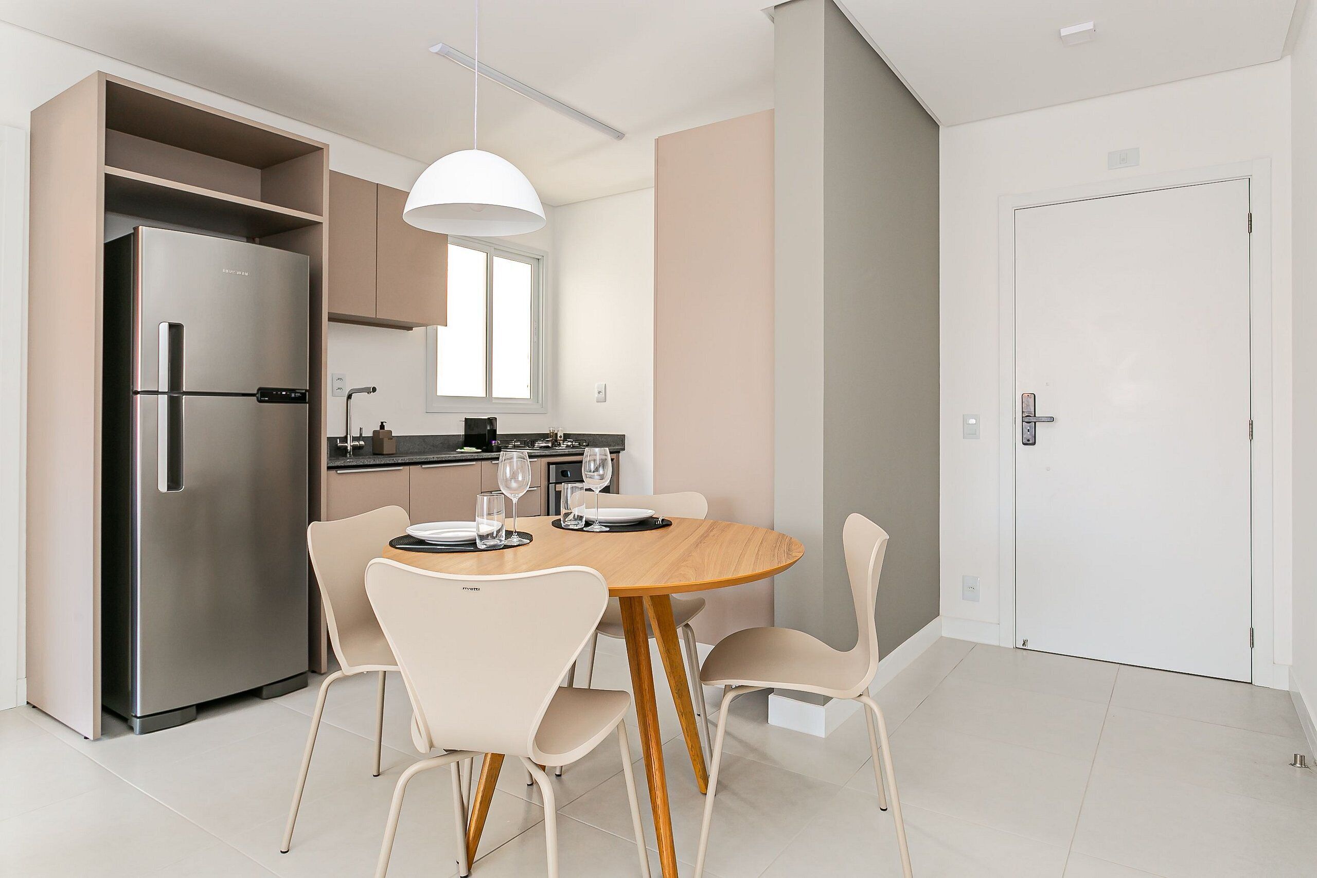A modern kitchen with a built-in refrigerator, a dining table with chairs, and a pendant light.