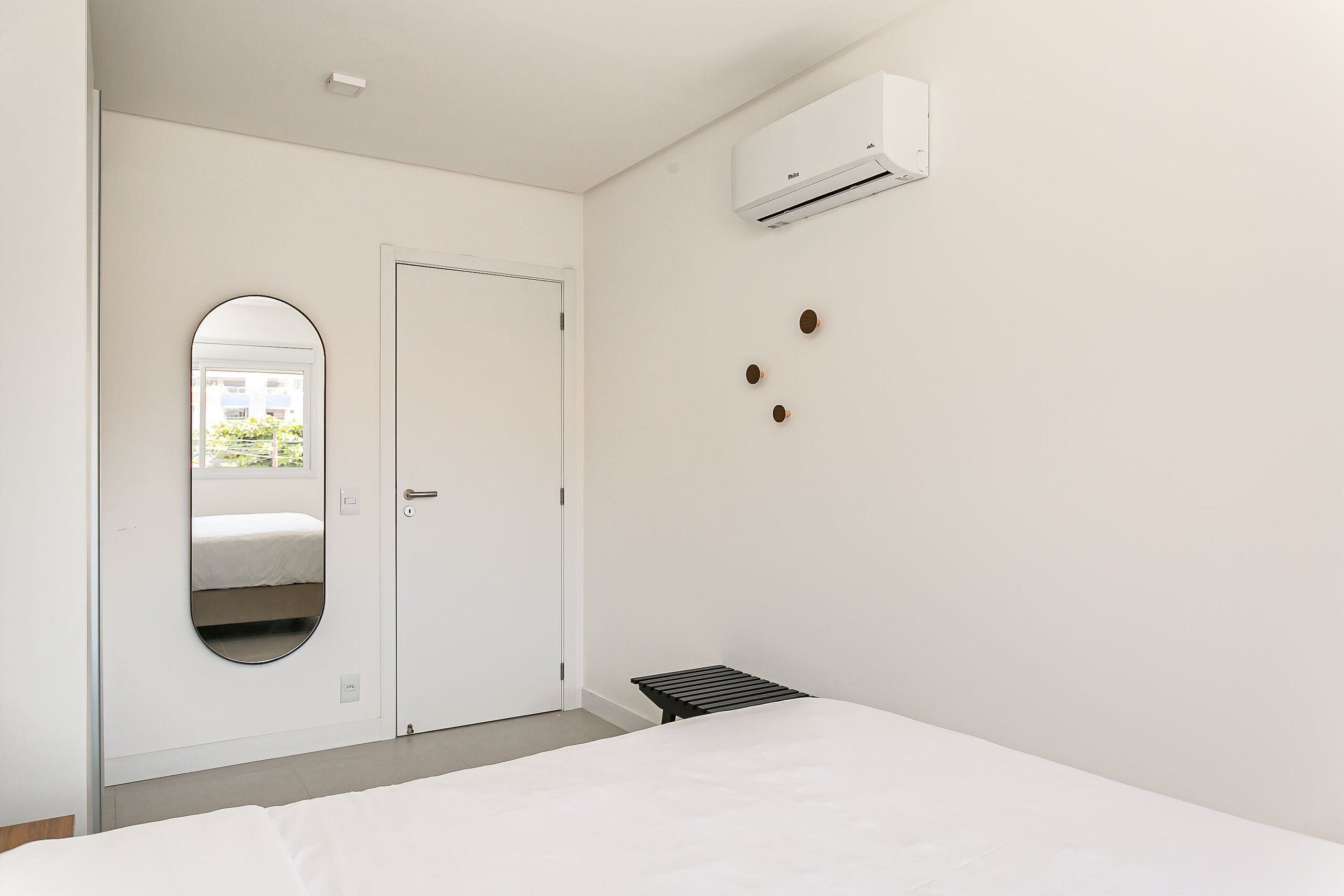 A minimalist bedroom with a bed, a white door, a small table, and an air conditioning unit on the wall.