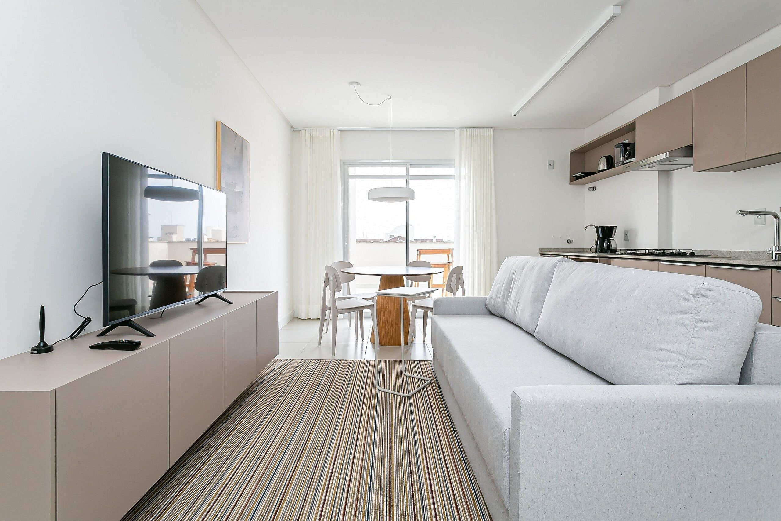 A modern living room with a flat-screen TV, a sofa, and a dining area with a table and chairs.