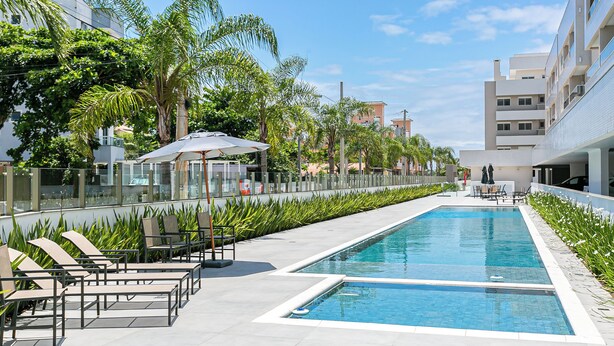 A swimming pool with lounge chairs, a glass railing, and palm trees. - Cannes Club by Viva - Residence a 200m da praia | Ingleses do Rio Vermelho (Florianópolis)