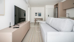 A modern, well-lit living room with a flat-screen TV, a sofa, and a dining area with a table and chairs. - Cannes Club by Viva - Residence a 200m da praia | Ingleses do Rio Vermelho (Florianópolis)
