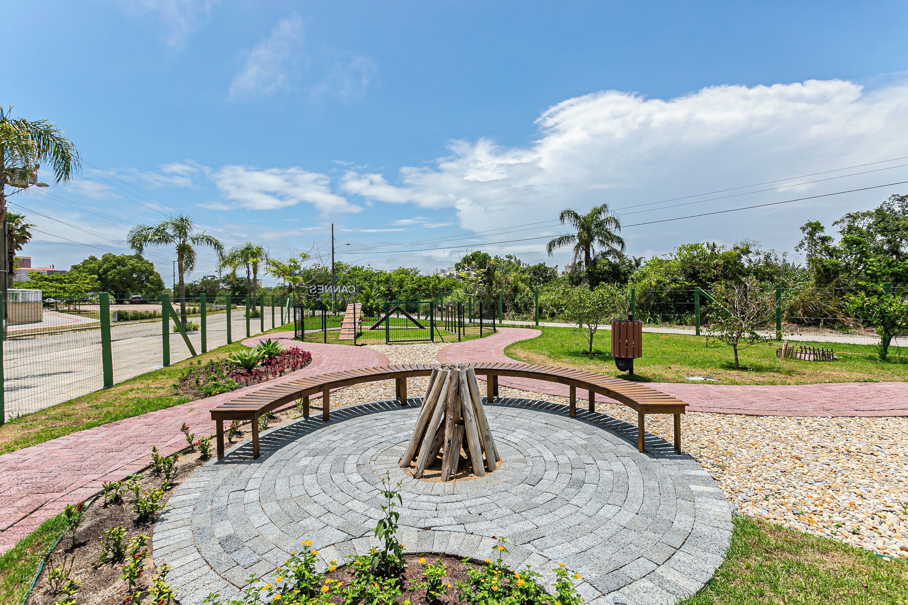 A circular stone plaza with benches, surrounded by a fence and greenery.