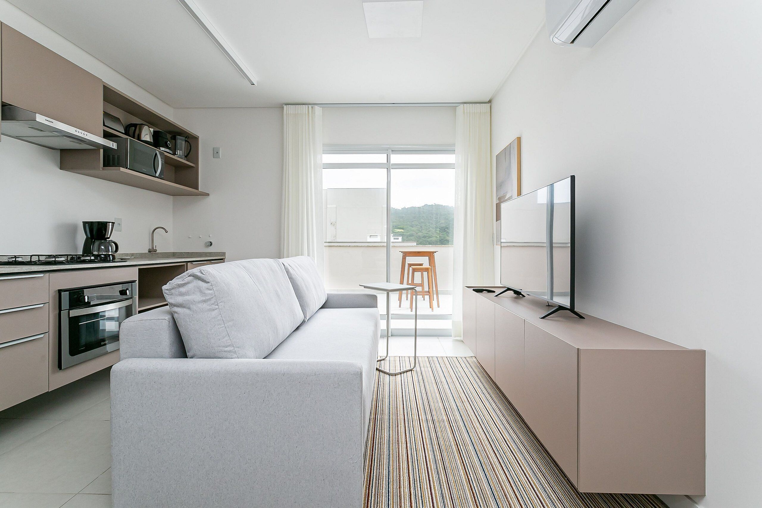 A modern kitchen with built-in appliances, a sofa, a TV, and a dining area with a view.