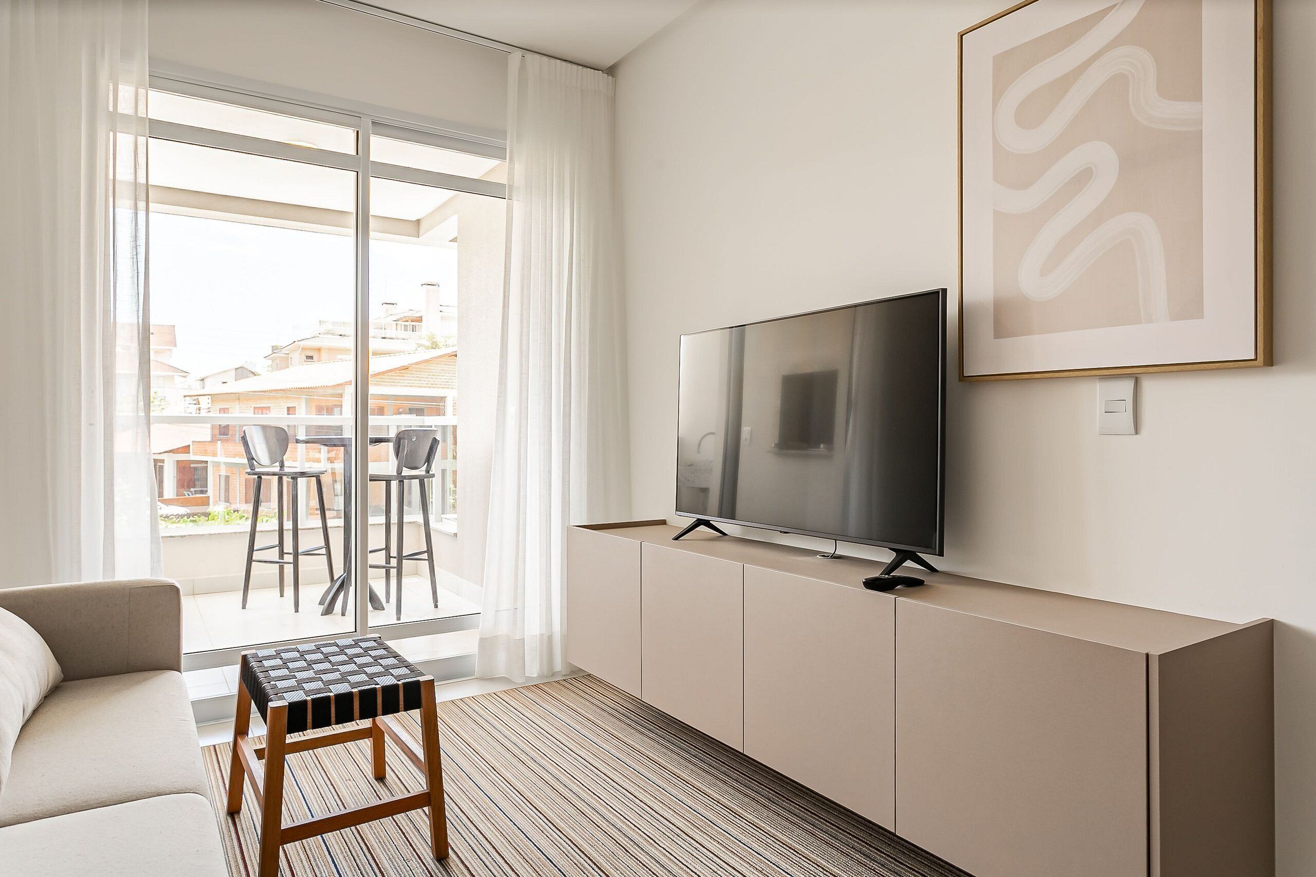 A modern living room with a sofa, a coffee table, a TV on a cabinet, and a large window with curtains.