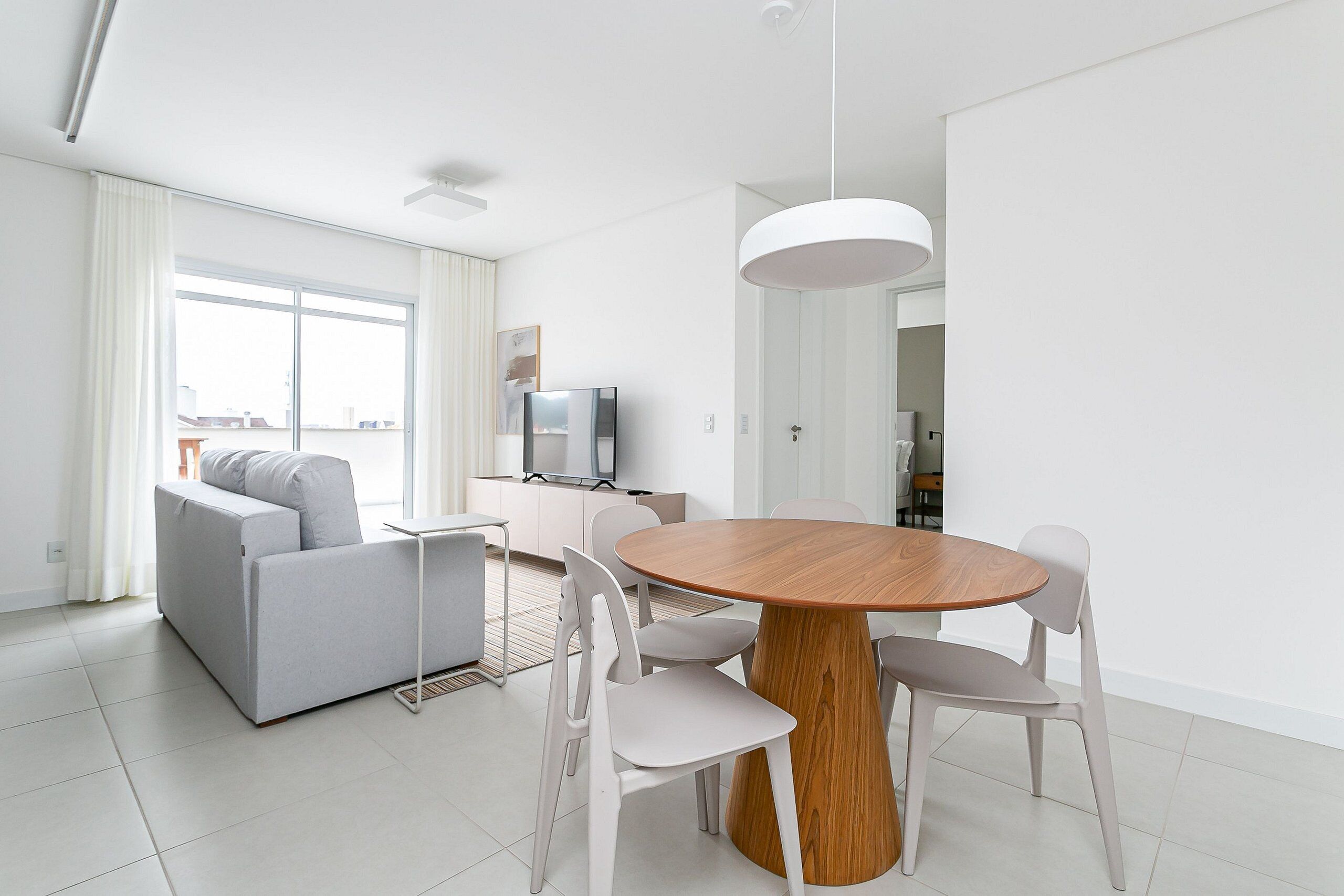 Un salón moderno con un sofá gris, una mesa de comedor redonda de madera y sillas blancas.