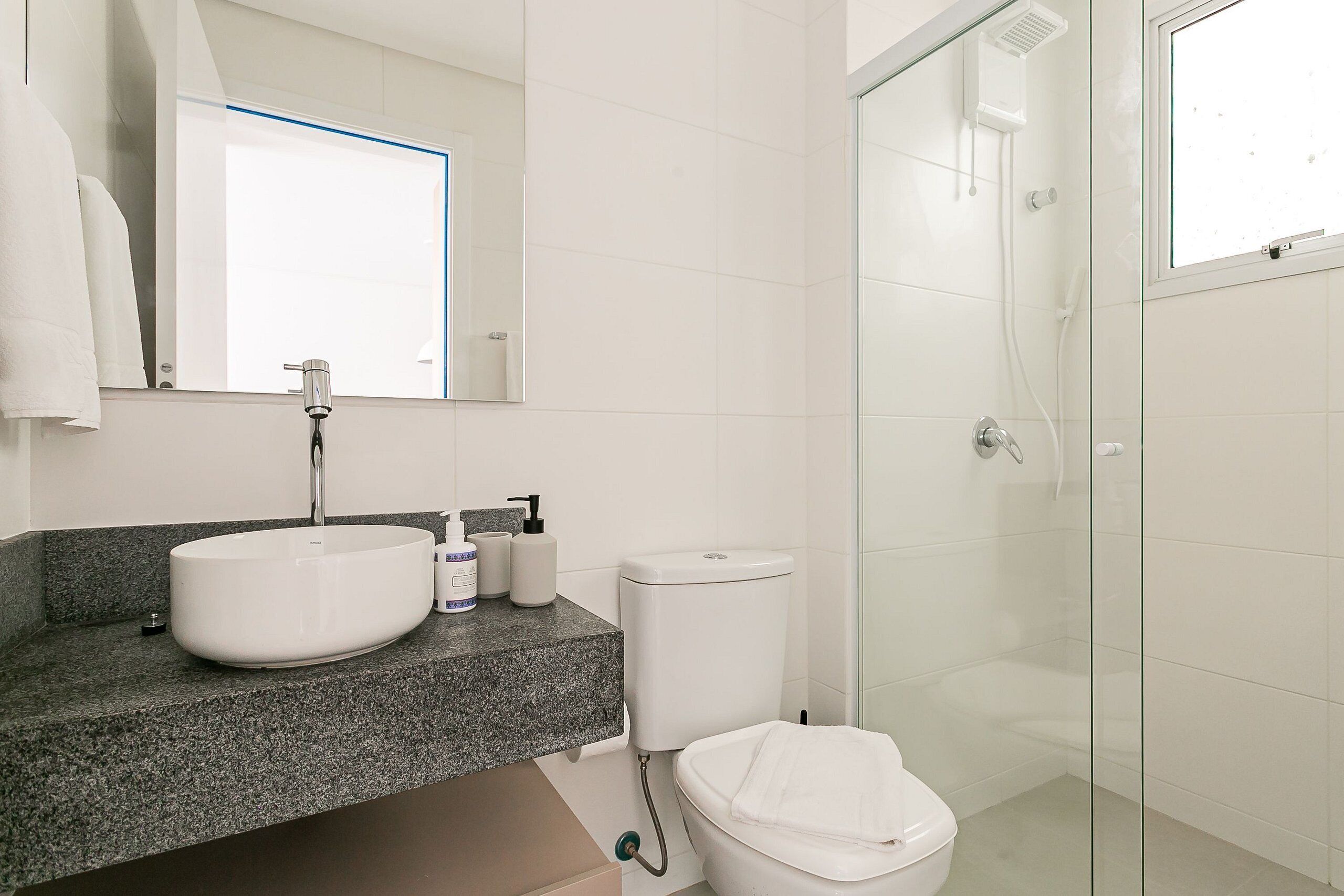 A modern bathroom with a granite countertop, a white sink, a toilet, and a glass shower enclosure.
