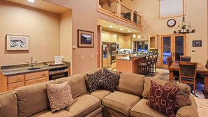 Una sala de estar acogedora con un sofá modular, una cocina con armarios de madera y un comedor con mesa y sillas.