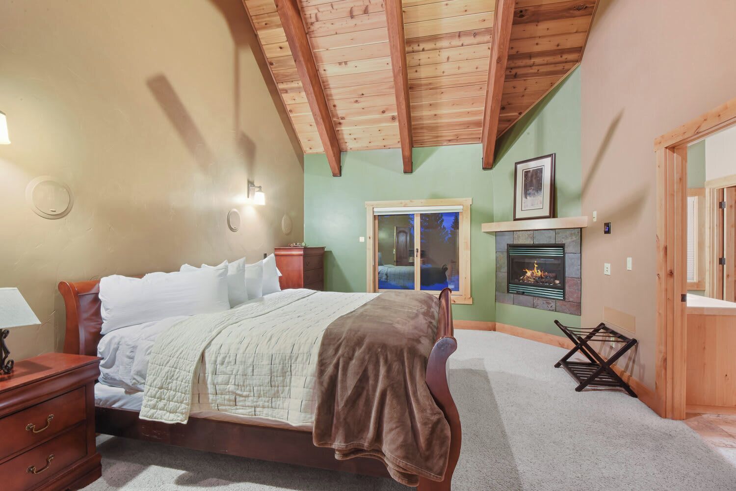 A bedroom with a bed, a nightstand, a dresser, a fireplace, and a window with a view.