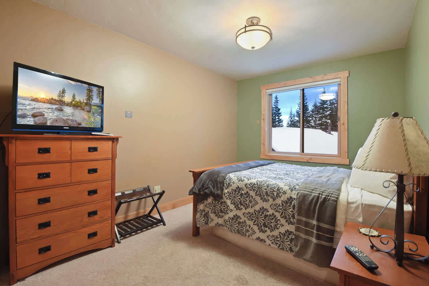 A bedroom with a bed, dresser, television, window, and lamp.