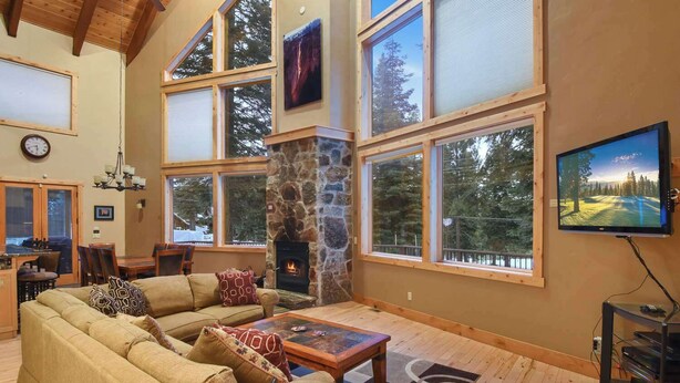 Amplia sala de estar con chimenea de piedra, ventanas grandes, televisor y un rincón de descanso acogedor.