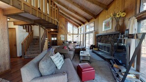 A spacious living area with a fireplace, a staircase, and a large window providing natural light. - Spacious Cabin Vibe w/ lots of Wood - Easy walk/ride to Village, Lodge and River (Sunriver)