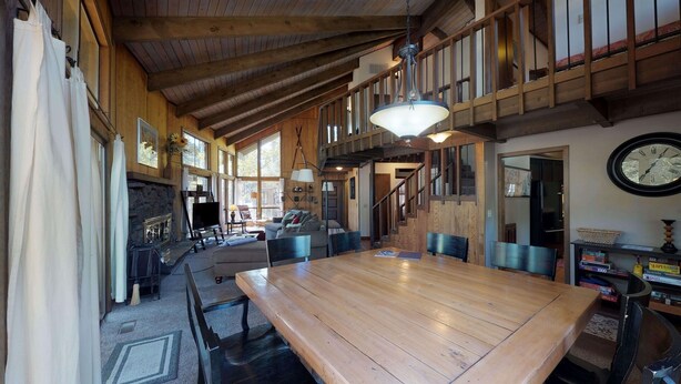 A spacious dining area with a large wooden table, surrounded by chairs, and a staircase leading to an upper level. - Spacious Cabin Vibe w/ lots of Wood - Easy walk/ride to Village, Lodge and River (Sunriver)