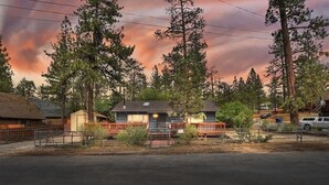 A two-story house with a porch, surrounded by tall trees and a cloudy sky. -  AC, Walk 2 Lake, Go Karts, Dining & Shops, King Bed, 55" TVs+Fenced Yard 4 Pet! (Big Bear)