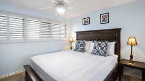 Une chambre à coucher avec un grand lit, deux cadres photos accrochés au mur, un ventilateur de plafond et une table de chevet avec une lampe.