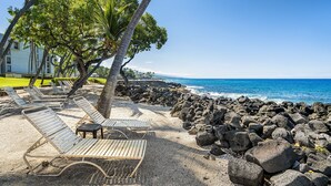 Une plage avec des chaises longues, des palmiers et une côte rocheuse.