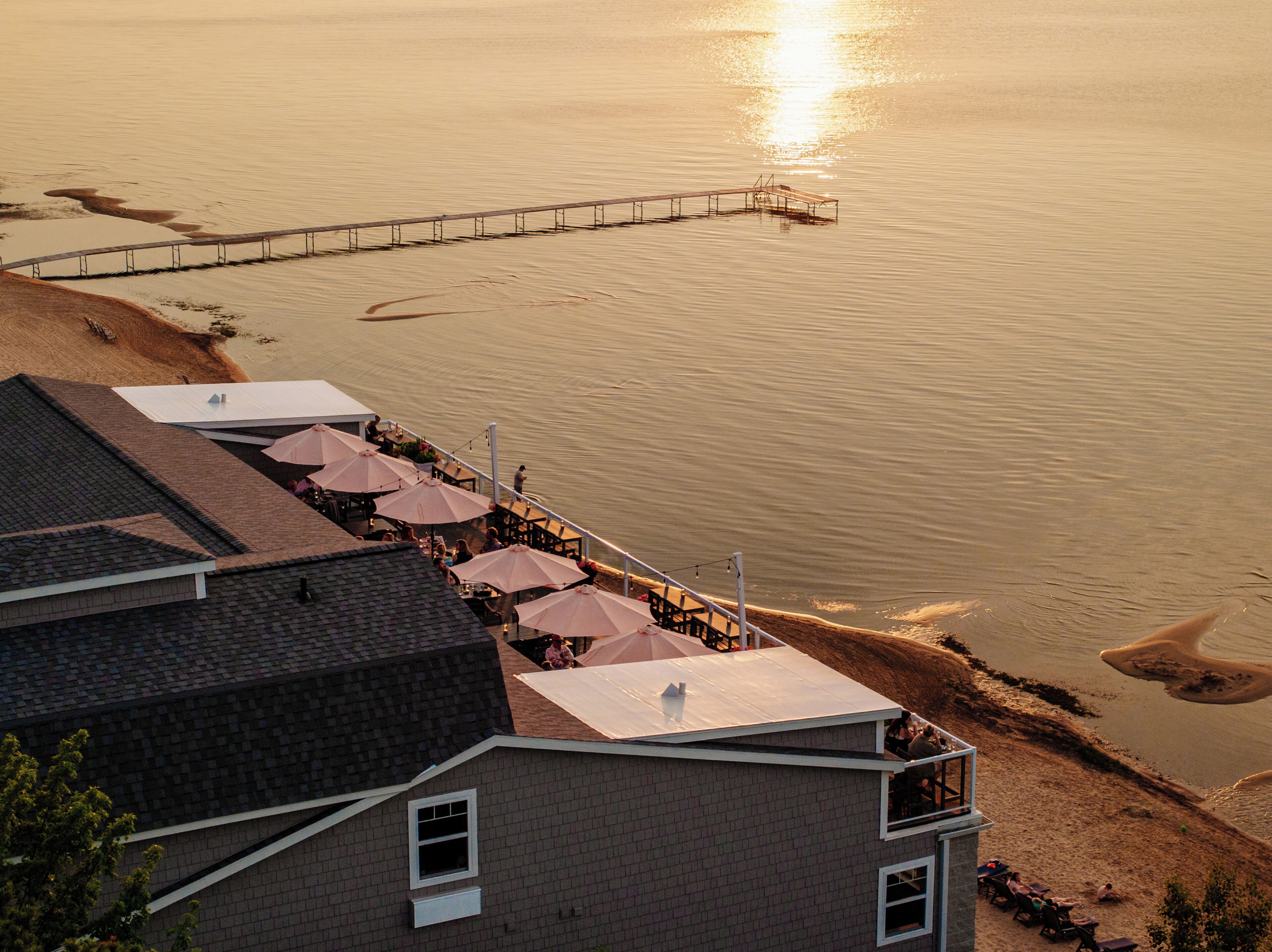 A beachfront property with a patio area featuring umbrellas and outdoor seating.