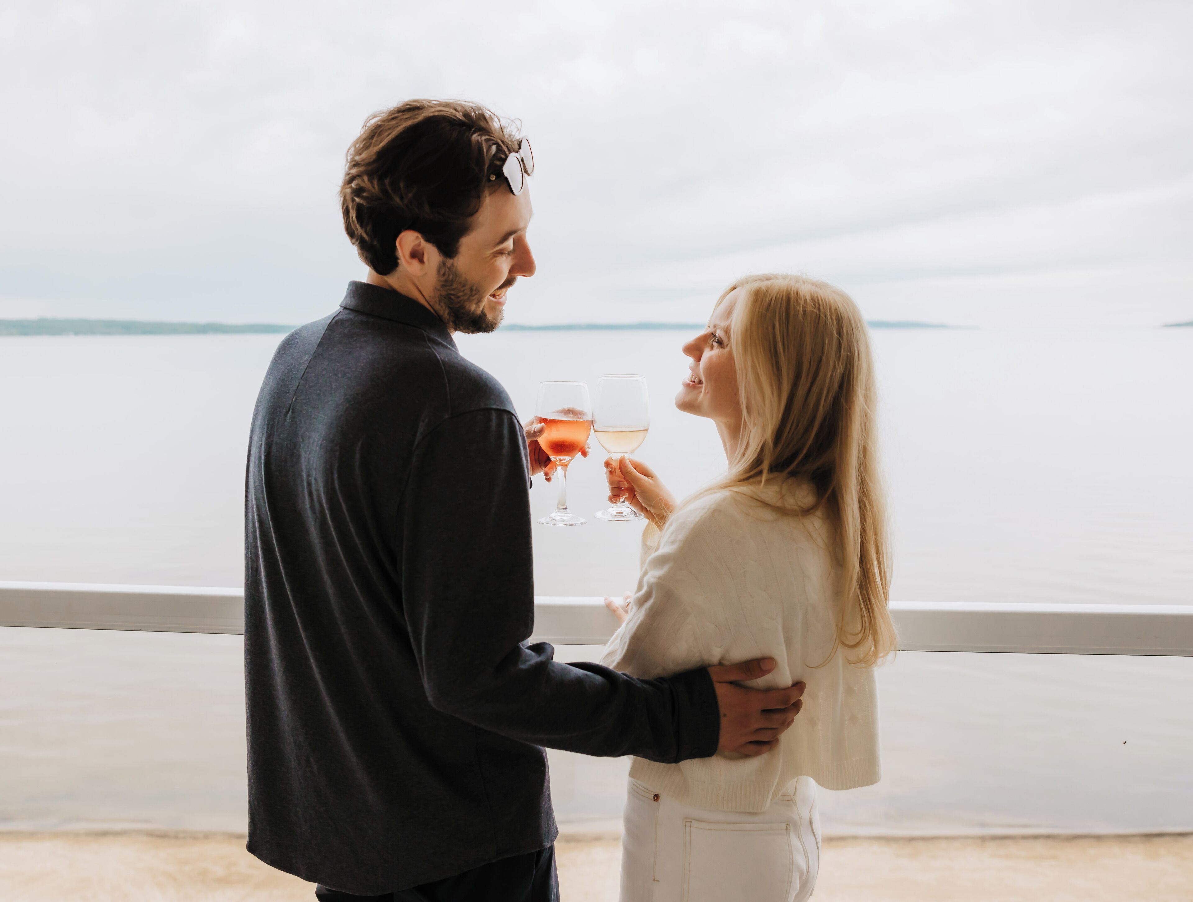 Um casal em pé junto a um corrimão, com vista para a água.