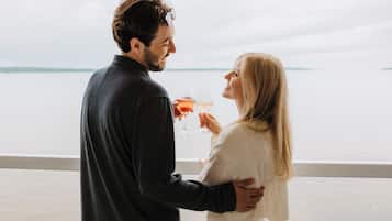 Um casal em pé junto a um corrimão, com vista para a água.