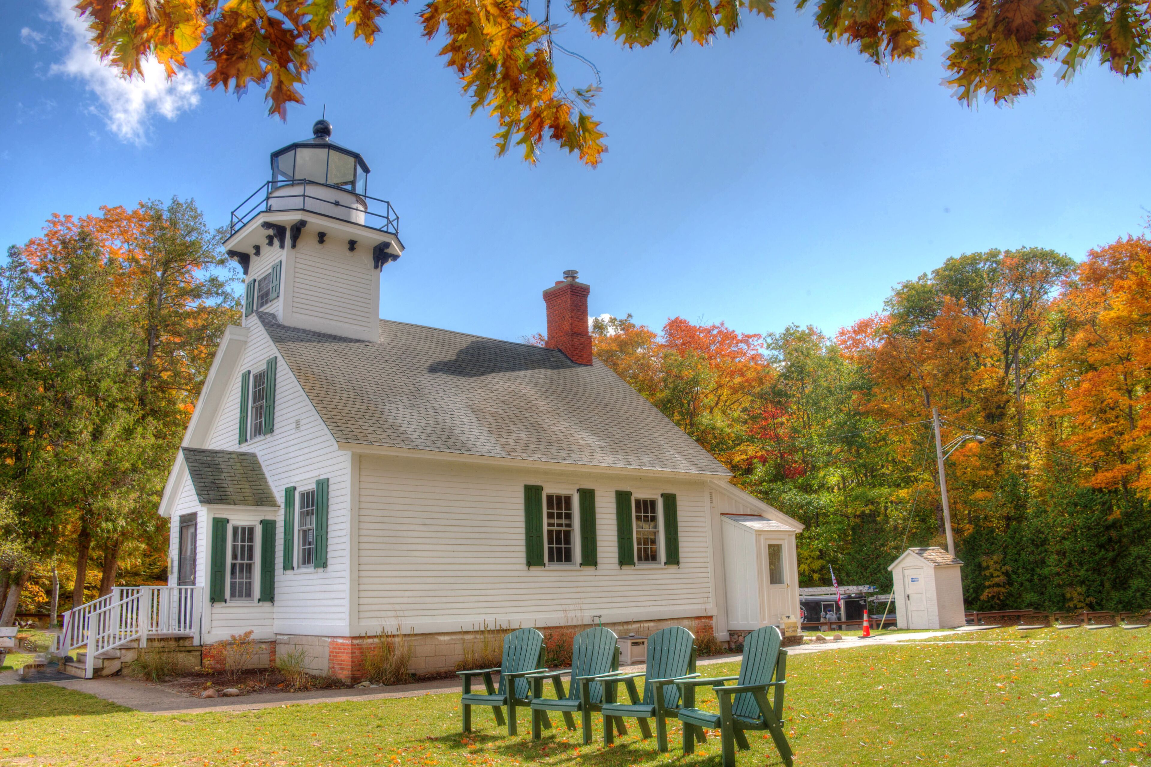 A white building with a lighthouse tower, green shutters, and a small adjacent structure.