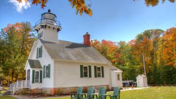 A white building with a lighthouse tower, green shutters, and a small adjacent structure.