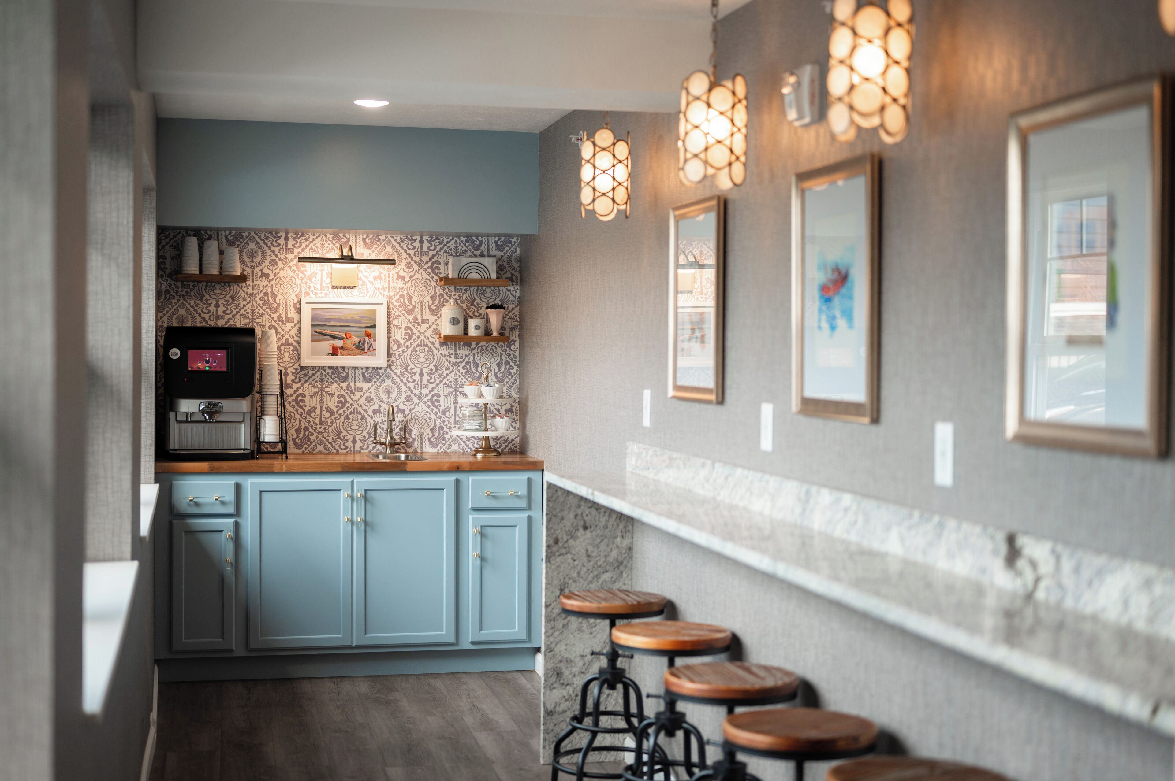 A modern kitchen with blue cabinets, a coffee machine, and bar stools.