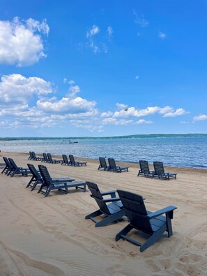 A beach with rows of lounge chairs and a clear view of the ocean. - Alexandra Inn (Traverse City)