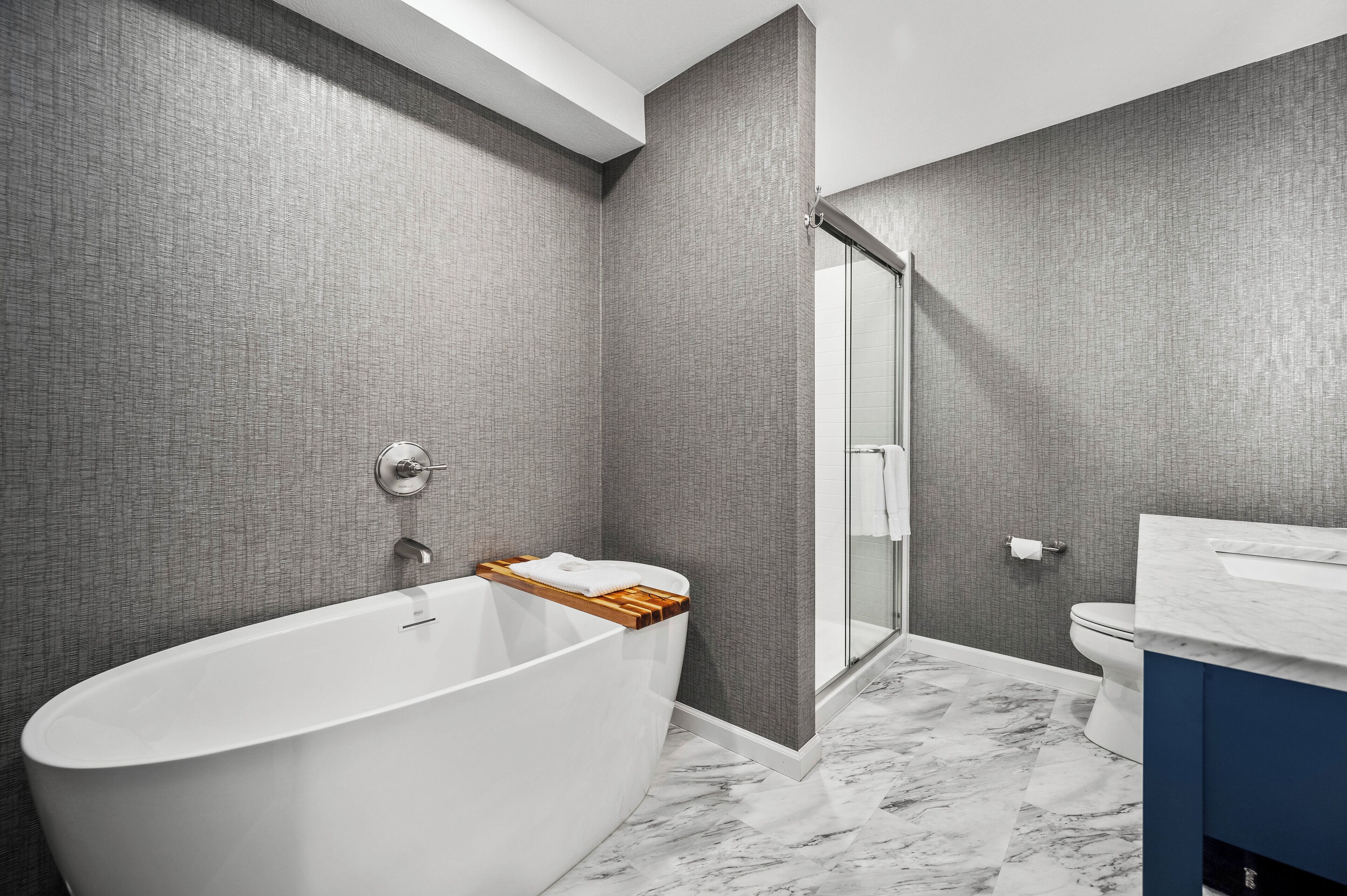 A modern bathroom with a freestanding bathtub, a glass shower enclosure, and a marble floor.
