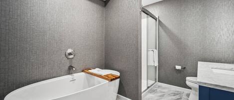 A modern bathroom with a freestanding bathtub, a glass shower enclosure, and a marble floor.