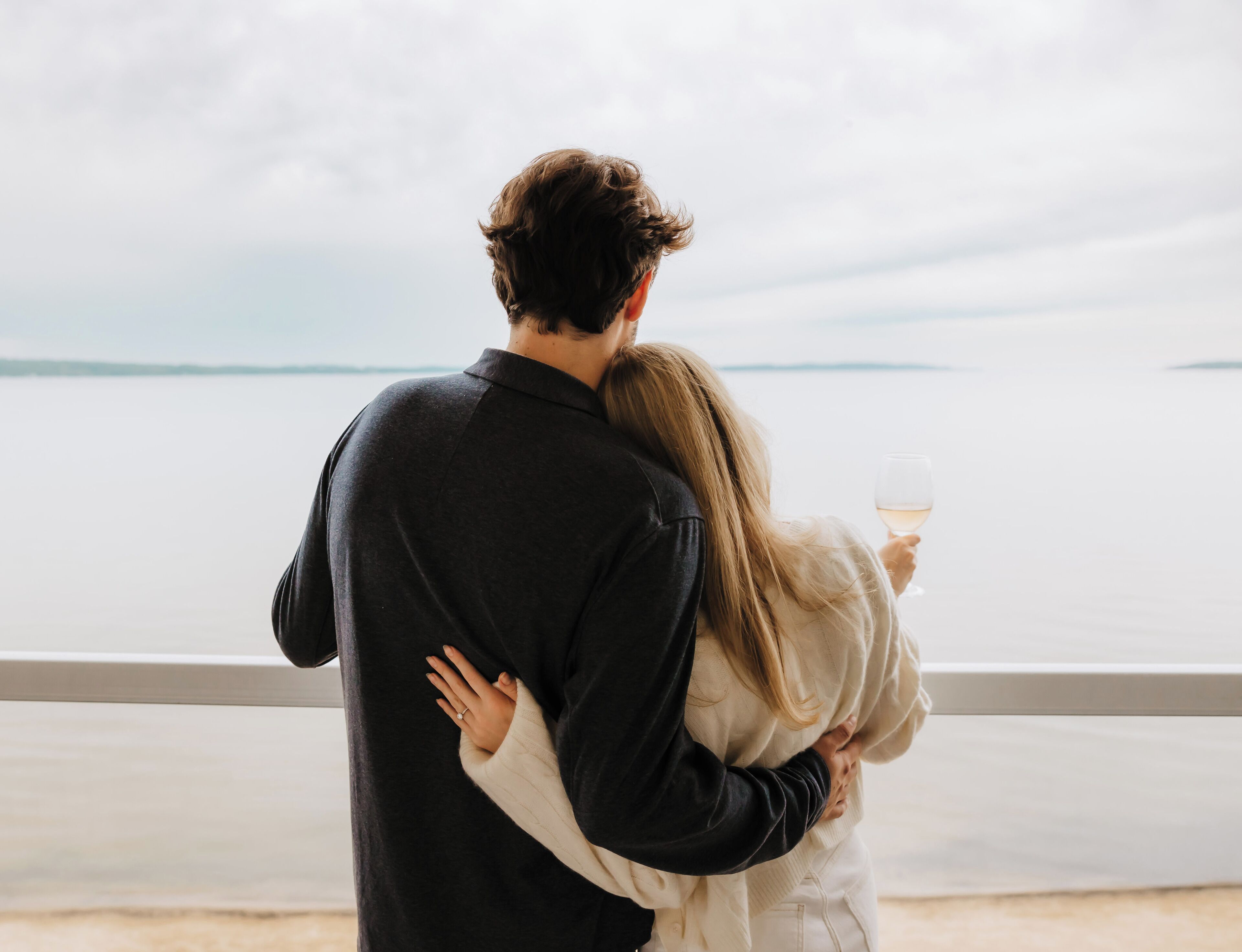 Un couple s’embrasse près d’une balustrade, avec une étendue d’eau en contrebas.