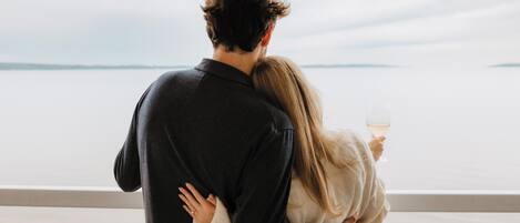 Un couple s’embrasse près d’une balustrade, avec une étendue d’eau en contrebas.