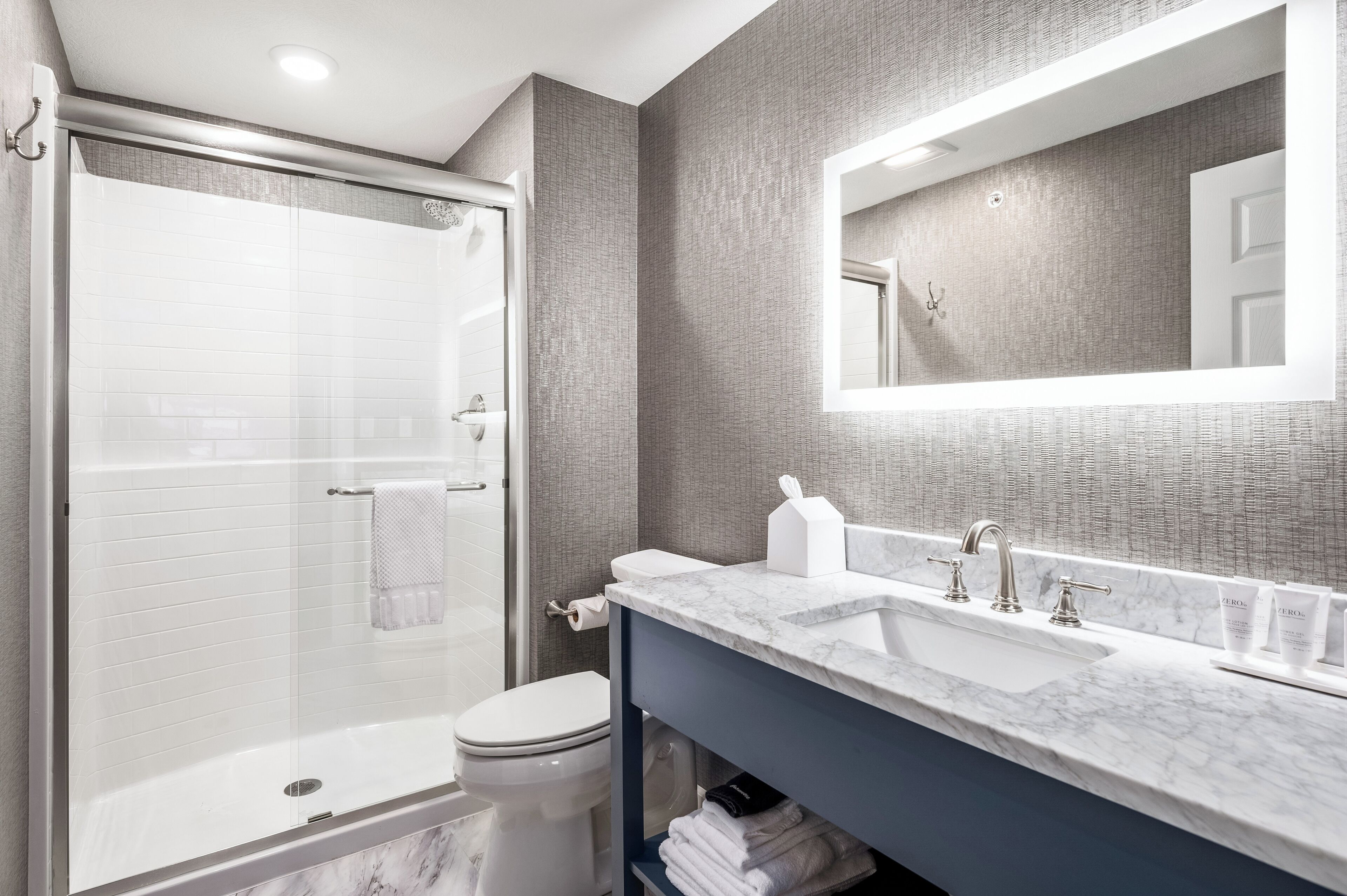 A modern bathroom with a glass-enclosed shower, a white toilet, a marble sink, and a large mirror.