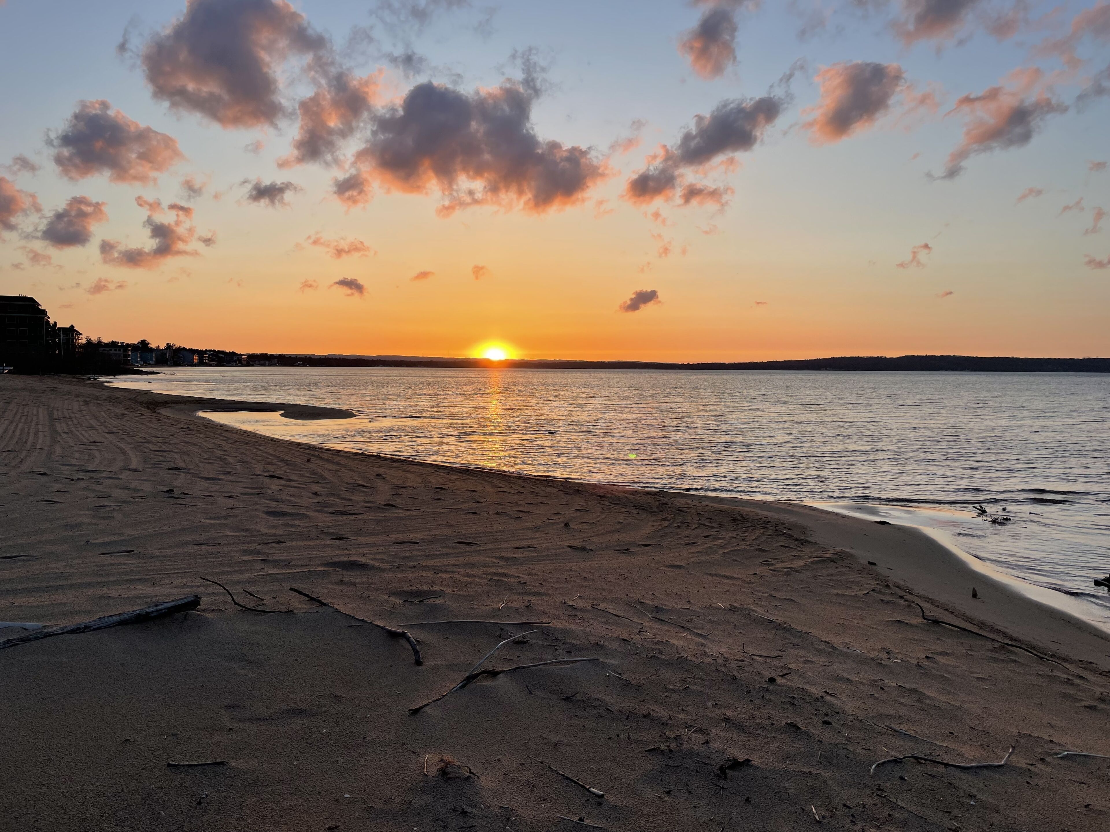 A beach with a sunset, sandy shore, and calm sea.