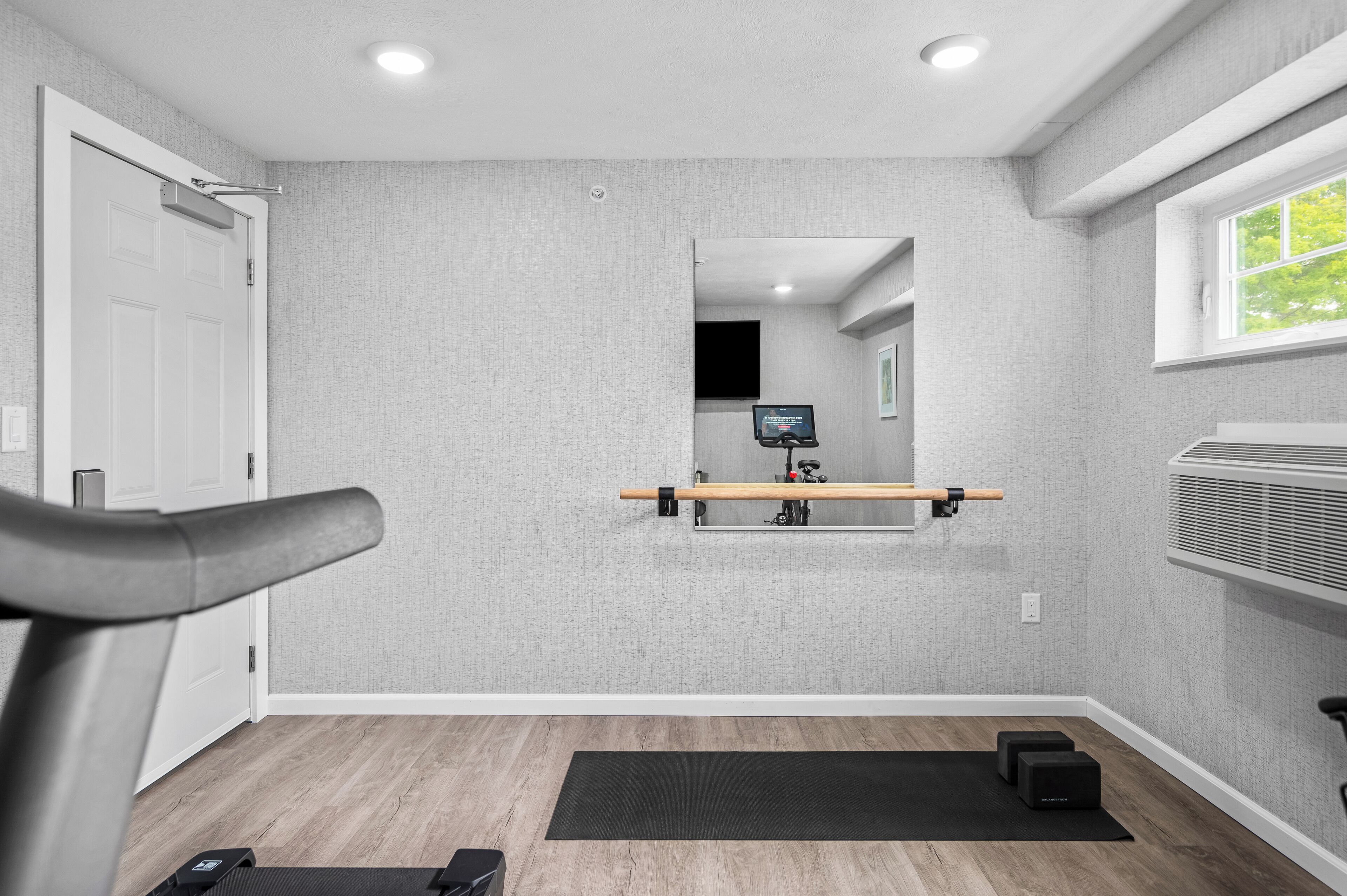A room with a treadmill, a mirror, a TV, and a window.