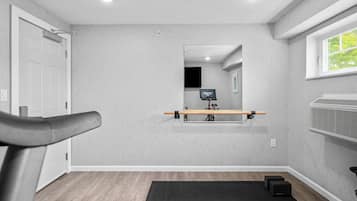 A room with a treadmill, a mirror, a TV, and a window.