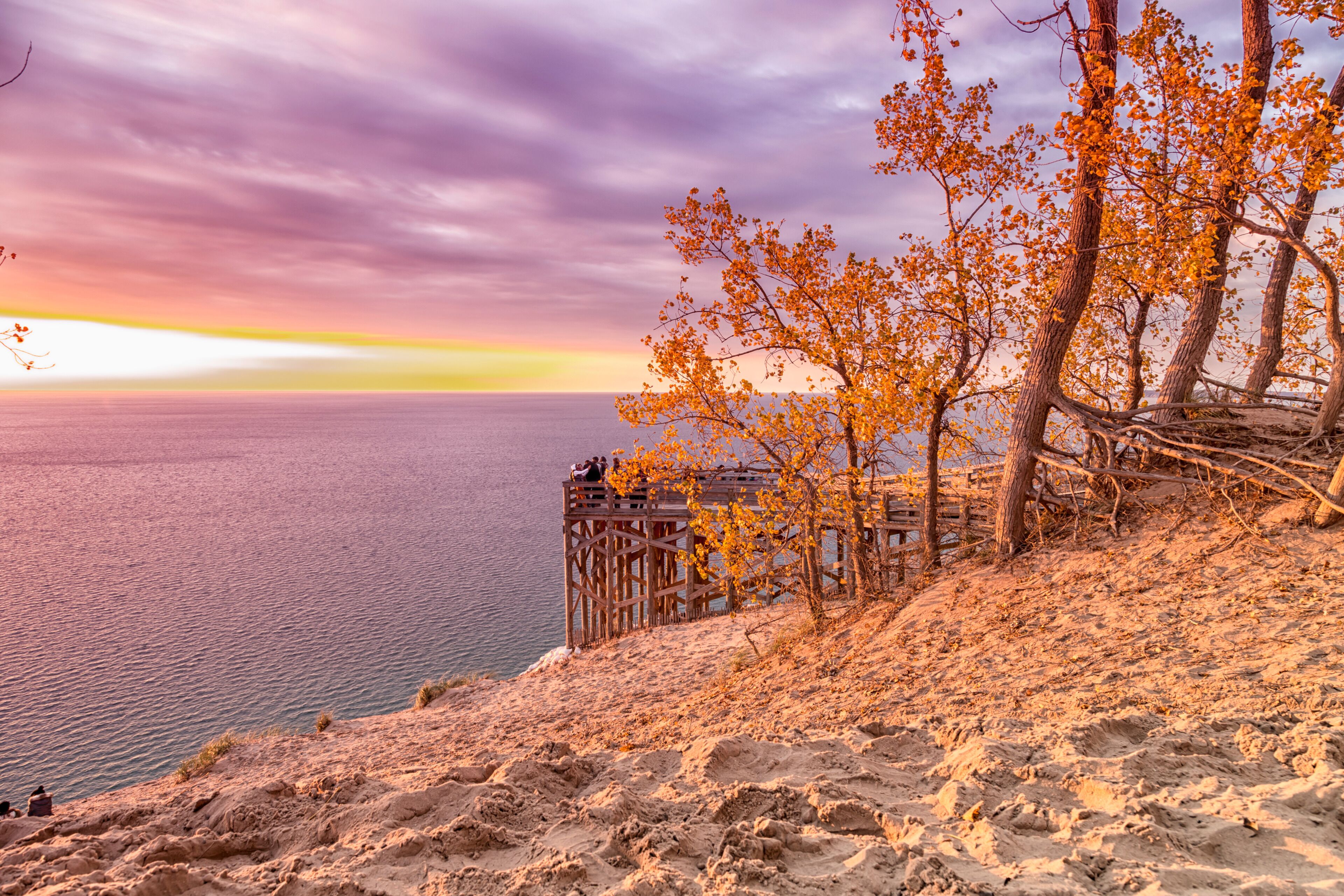 A wooden pier extending into a body of water, with autumn-colored trees and a clear sky.